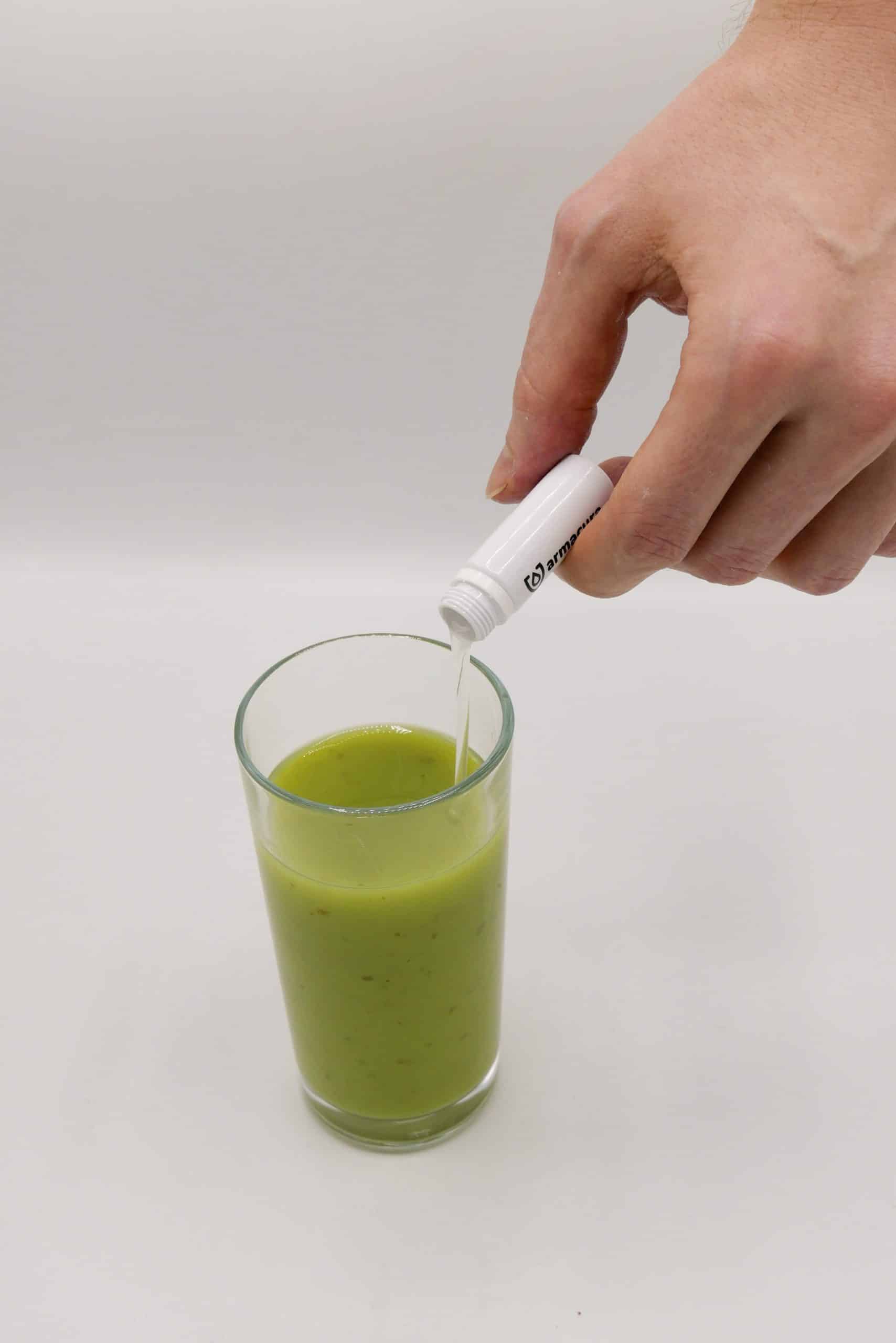 Nahaufnahme von Hand mit armacura Ampulle, die in ein Glas grünen Smoothie geschüttet wird